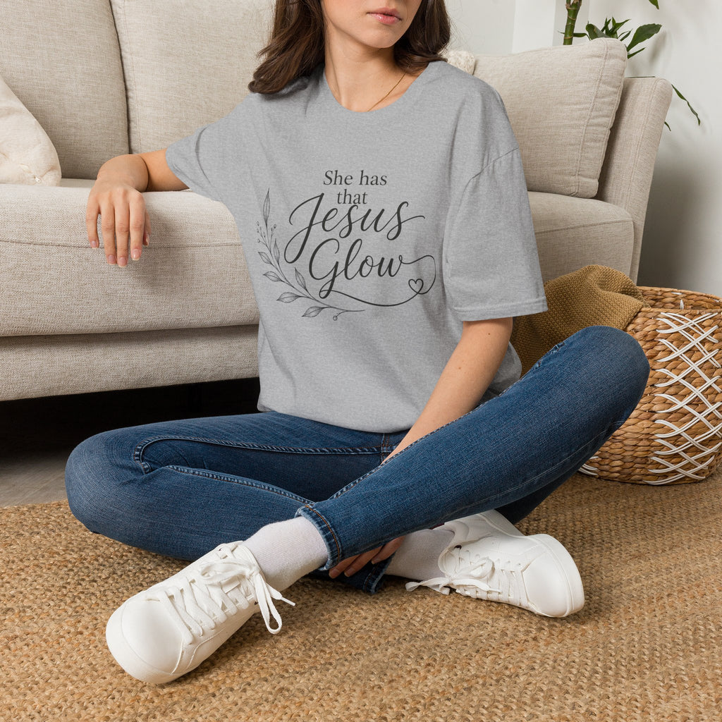 Lightweight cotton tee with 'She Has That Jesus Glow' botanical script design in soft, hopeful typography.