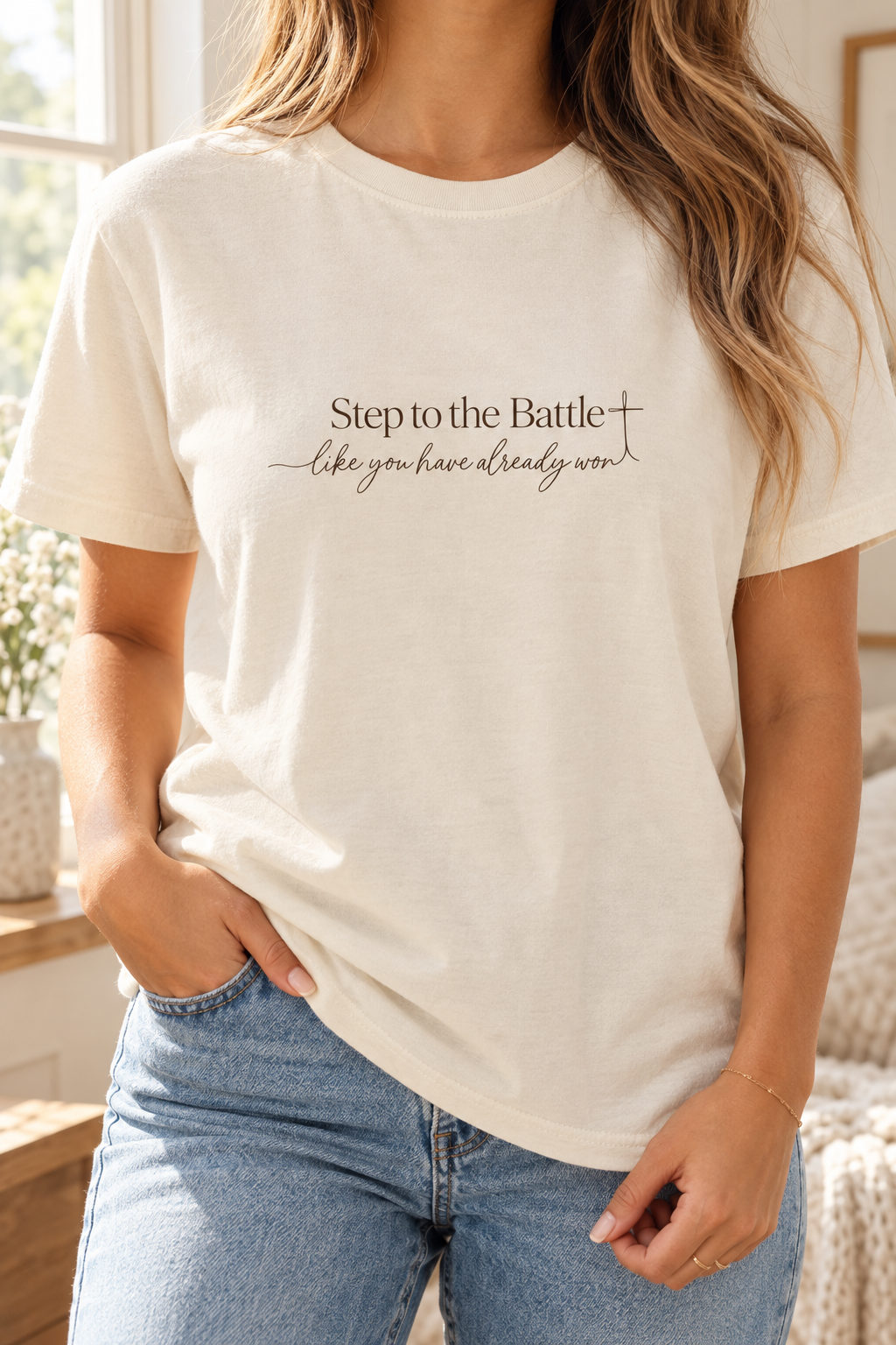 A woman wearing a cream-colored short-sleeve t-shirt with the text 'Step to the Battle like you have already won' printed in black script on the chest, paired with blue jeans | Faithful Finds