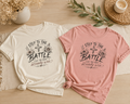 Boxy pigment-dyed tee with floral cross design and 'Step to the Battle Like You Have Already Won' hand-lettered faith message